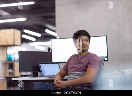 Portrait of young indian successful male software developer sitting on desk at modern startup office Stock Photo