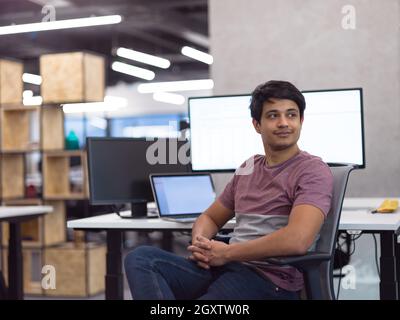 Portrait of young indian successful male software developer sitting on desk at modern startup office Stock Photo