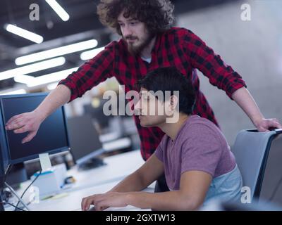 two young male software developers using laptop and desktop computer while writing programming code at modern creative startup office Stock Photo