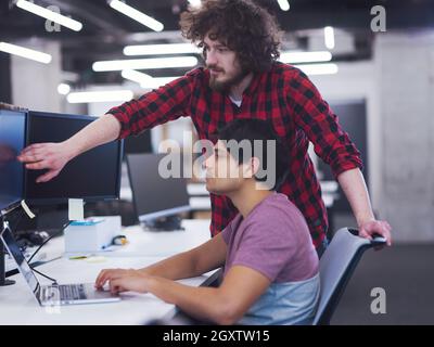 two young male software developers using laptop and desktop computer while writing programming code at modern creative startup office Stock Photo