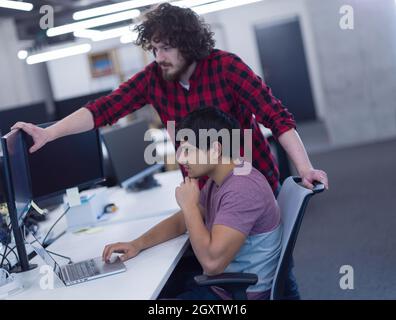 two young male software developers using laptop and desktop computer while writing programming code at modern creative startup office Stock Photo