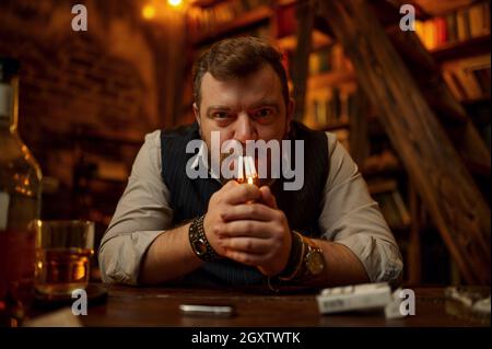 Crazy man smokes three cigarettes at the same time, vintage office interior on background. Tobacco smoking culture. Bad habit and addiction Stock Photo