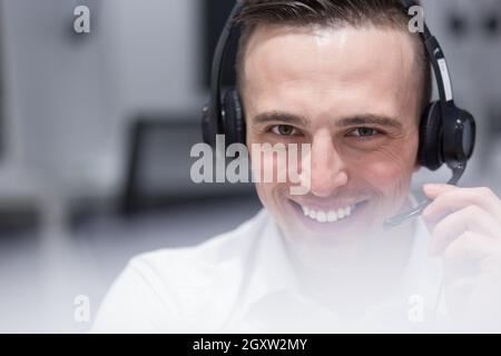 young smiling male call centre operator doing his job with a headset Stock Photo