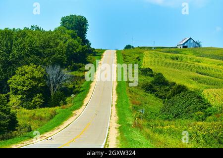 Empty old road through hills with barn and corn fields Stock Photo