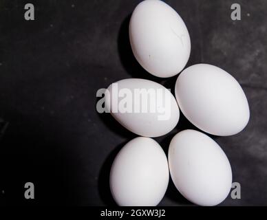 Five fresh white eggs lying down on black surface Stock Photo