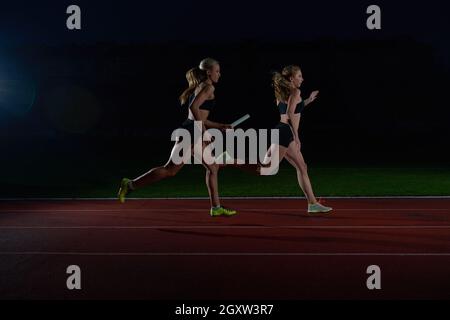 woman athletic runners passing baton in relay race Stock Photo