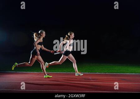 woman athletic runners passing baton in relay race Stock Photo