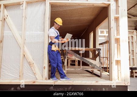 Cheerful male builder using laptop at construction site Stock Photo