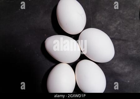 Five fresh white eggs lying down on black surface Stock Photo