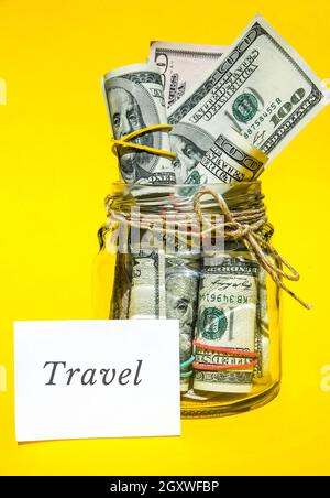 Glass jars filled with dollar bills, savings inside glass jar, money isolated on yellow background. Paper note written word TRAVEL . Business budget o Stock Photo
