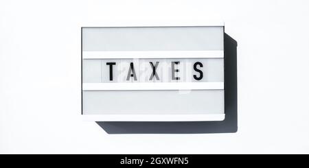 Lightbox board on a white background with the words TAXES in black letters. Currency, cash Stock Photo