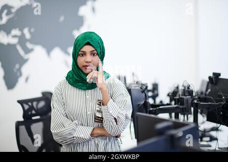 Portrait of muslim african female software developer with green hijab standing at modern open plan startup office Stock Photo