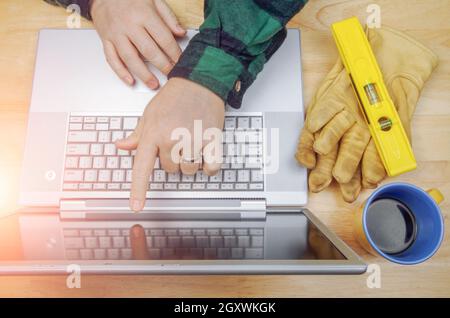 Work Gloves, Level Next To Contractor Pointing and Reviews Project on Laptop Computer. Stock Photo