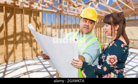 Hispanic Male Contractor Talking with Female Client Over Blueprint Plans At Construction Site. Stock Photo
