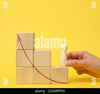 female hand holds a wooden figurine on a ladder of cubes on a jelly background. Career growth concept, promotion, personal growth, coach help Stock Photo