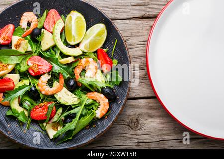 Salad with shrimps,strawberries,avocado and herbs.Seafood salad on rustic wooden background.Flat lay Stock Photo