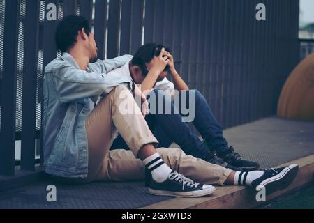 Sad Depressed two Insomnia Men. Sitting on the street sidewalk after lost job. Young jobless man suffering depression sitting on ground street undergr Stock Photo