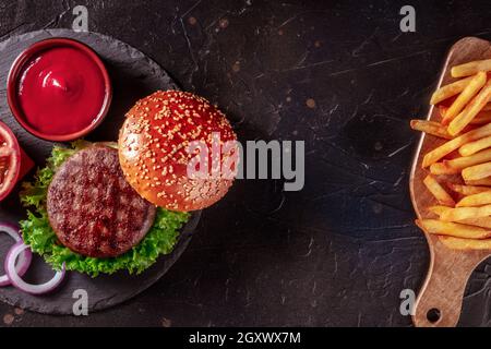 Burger and French fries, fast food background with copy space. Hamburger ingredients and fried potato, overhead flat lay shot on black Stock Photo