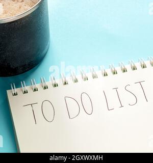 To do list square shot with handwriting in a notepad and a coffee mug on a blue background. The concept of planning, time management etc Stock Photo