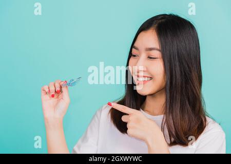 Portrait young Asian beautiful woman smiling pointing with finger silicone orthodontic retainers for teeth, Female hold teeth retaining tools after re Stock Photo