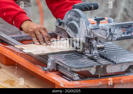 Worker Using Wet Tile Saw to Cut Wall Tile At Construction Site. Stock Photo