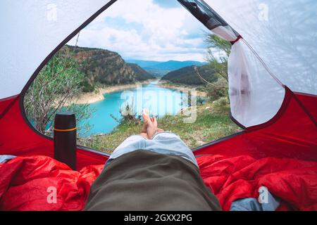 Man lying and relaxing in tent in nature. View from the inside of tent to the lake and mountains. Camping or with tent Stock Photo