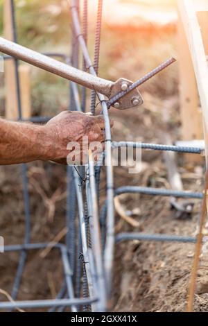 Worker Using Tools To Bend Steel Rebar At Construction Site. Stock Photo