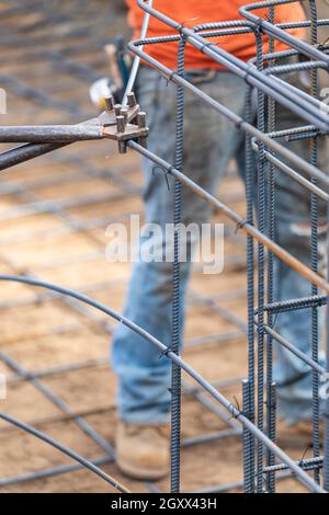 Worker Using Tools To Bend Steel Rebar At Construction Site. Stock Photo