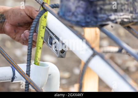 Plumber Using Level And Tape Measure While Installing PVC Pipe At Construction Site. Stock Photo