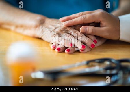 Younger Female Hands Touching Senior Adult Woman Hands Near Stethoscope and Medicine Bottle. Stock Photo