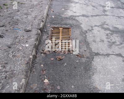 Rusty storm drain grate in cracked asphalt Stock Photo