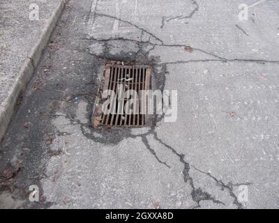 Rusty storm drain grate in cracked asphalt Stock Photo