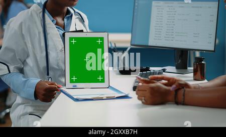 Close up of doctor vertically holding tablet with green screen on desk. Medical specialist showing mockup isolated template and background for chroma key on digital gadget in cabinet Stock Photo