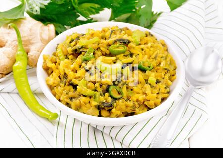 Indian national dish of kichari made of mung bean, rice, stalk celery, spinach, hot pepper and spices in a bowl on napkin, ginger on white wooden boar Stock Photo