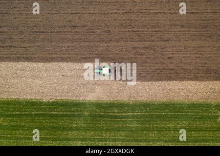 Aerial view of agricultural tractor tilling and harrowing ploughed field, directly above drone pov image of machinery working on farmland Stock Photo