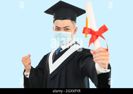 young male graduation wearing face mask and holding his college certificate during the coronavirus pandemic Stock Photo
