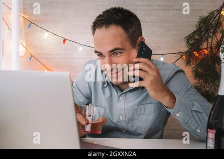 Office clerk celebrate Christmas at work. Celebrating Christmas and New Year in the workplace. An office worker drinks alcohol and calls on a smartpho Stock Photo