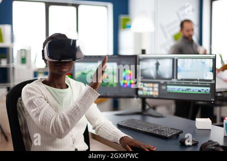 African video video maker experiencing VR headset, gesturing, editing video film montage working at footage and sound on computer with two displays. Videographer processing movie in creative agency Stock Photo