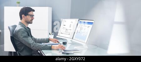 Young Businessman Looking At Invoice While Doing Online Banking On Computer Stock Photo