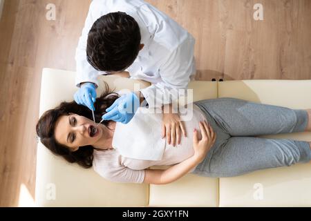 Dentist Treating Teeth Of Young Pregnant Woman Patient Lying In Clinic Stock Photo