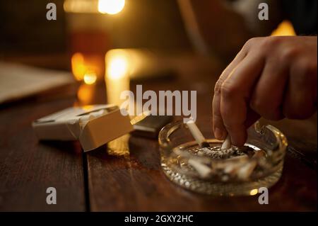 Man puts out a cigarette in an ashtray, closeup view. Tobacco smoking culture, specific flavor. Male smoker leisures in office Stock Photo