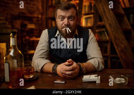 Crazy man smokes three cigarettes at the same time, vintage office interior on background. Tobacco smoking culture, specific flavor. Bad habit and add Stock Photo