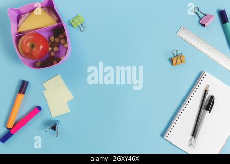 Primary school flat lay concept with assorted school supplies, notepad, pen, pencil, markets, stickers, paper clips and lunch box with sandwich, nuts Stock Photo