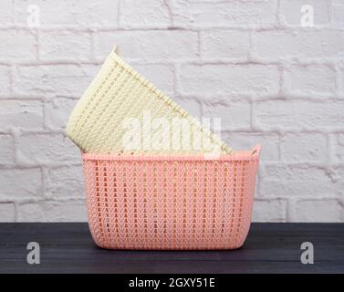 stack of plastic empty laundry baskets on wooden blue table. White brick wall background Stock Photo