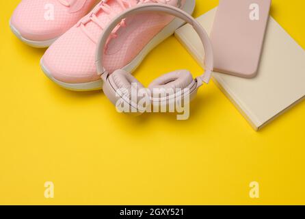 pair of pink sneakers, wireless headphones, a smartphone and a smart watch on a yellow background. Things and gadgets for sports, running Stock Photo