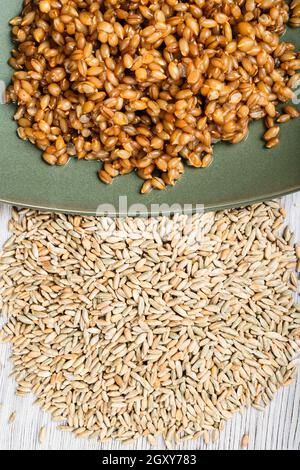 top view of raw whole rye grains and boiled porridge on green plate close up on wooden table Stock Photo