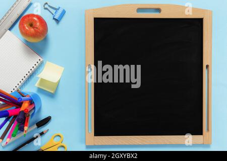 Flat lay with school concept on blue background with various schooling accessories, pens, pencil, notepad, paper clips, apple, ruler, scissors, empty Stock Photo