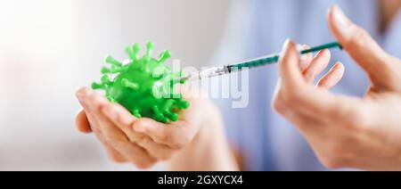 Medical worker holding a model of coronavirus and a syringe. Concept of vaccination aganst pandemic of Covid-19. Idea of fighting with pandemic. Stock Photo