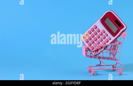 pink plastic calculator in a miniature pink trolley on a blue background. Budget planning concept, savings counting, cost control, banner Stock Photo