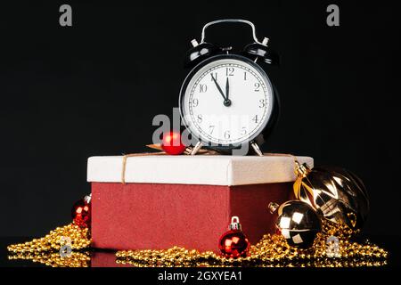 Black vintage alarm clock with christmas baubles and decor on dark black background. Christmas eve concept Stock Photo
